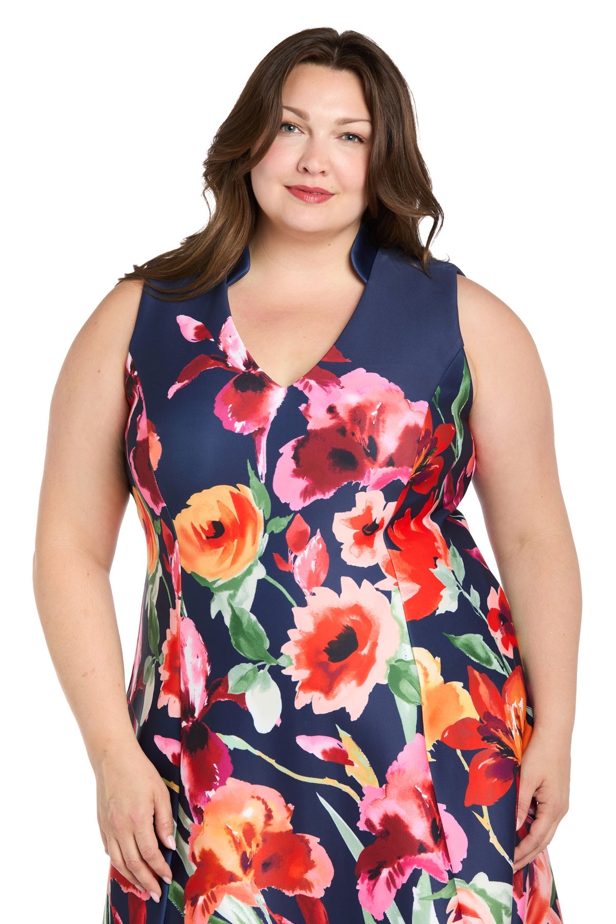 A woman stands facing the camera and smiles, wearing the R&M Richards 4056W Plus-Size Wedding Guest Dress—a knee-length, sleeveless piece featuring a bold, colorful floral pattern.